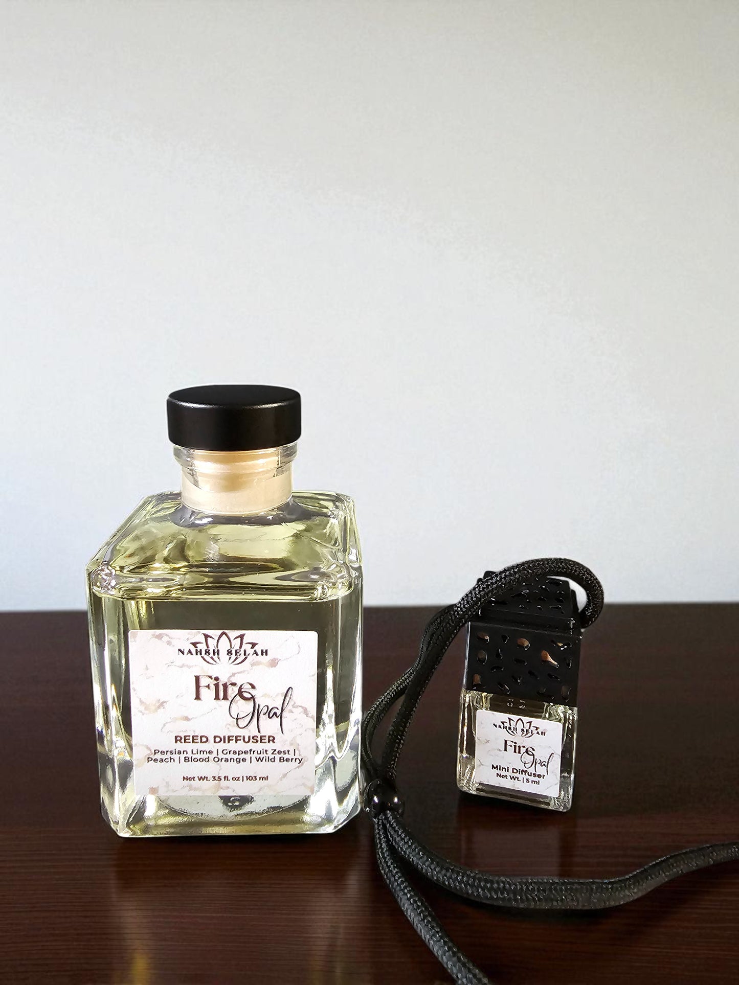 Two bottles of fragrance on a wooden surface with a light gray background, one large and one mini bottle.