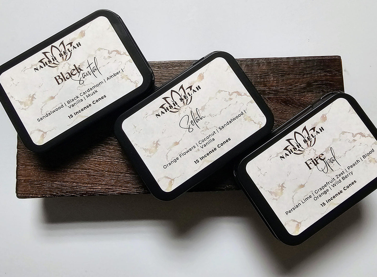 Three black tins of incense cones on a wooden block.