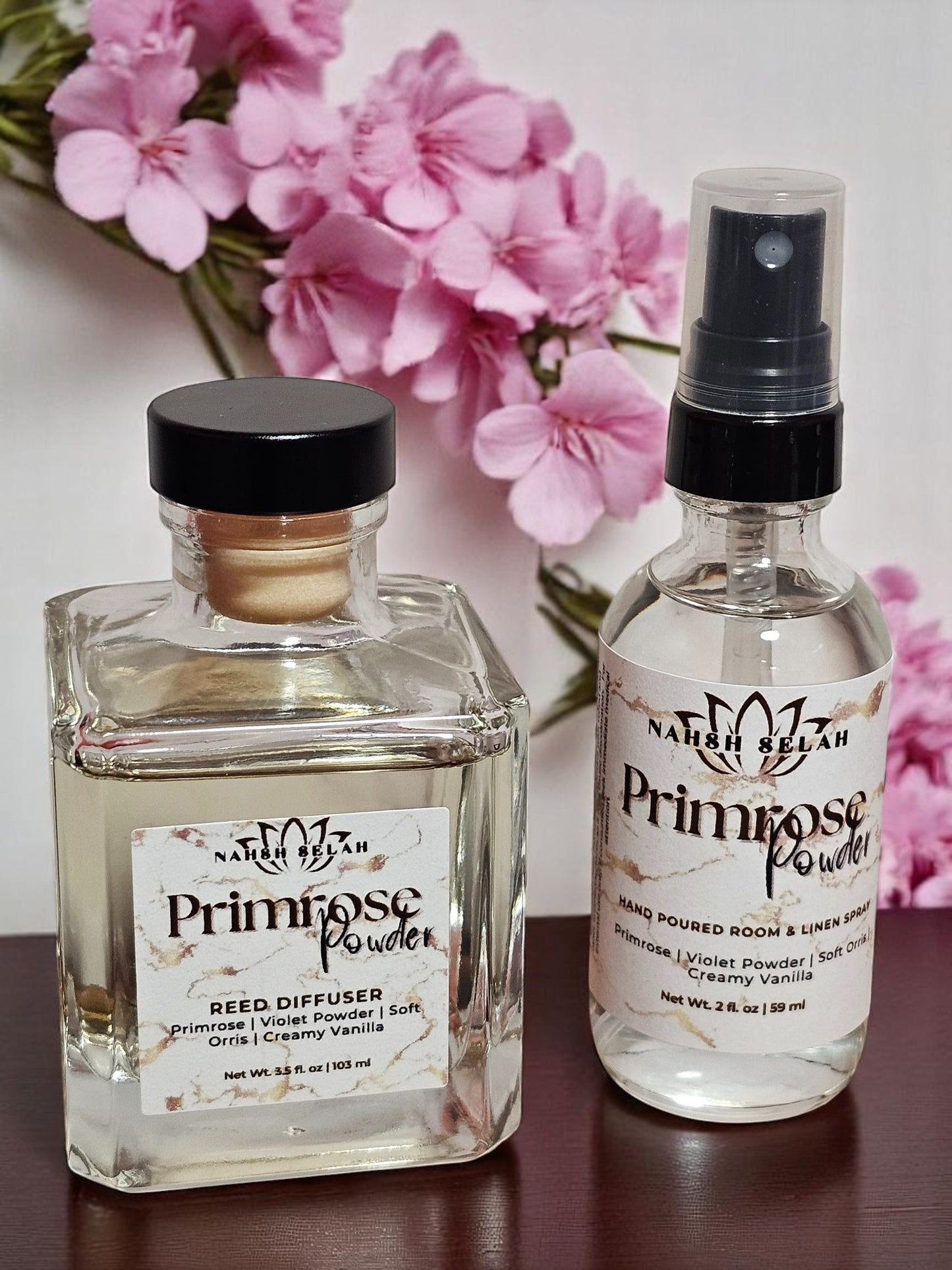 Two bottles of with pink flowers in the background.
