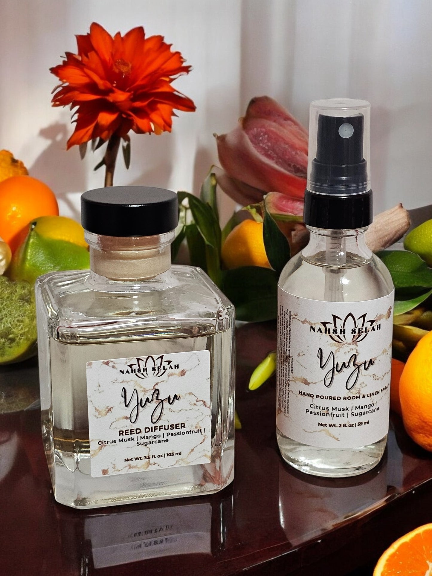 Two glass bottles with labels on a surface with fruits and flowers in the background