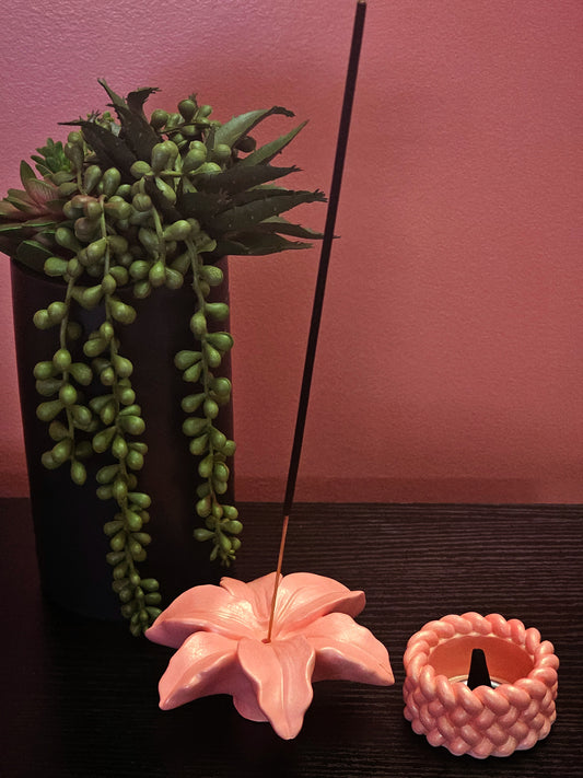 Pink flower-shaped incense holder with green plant and pink wall in the background