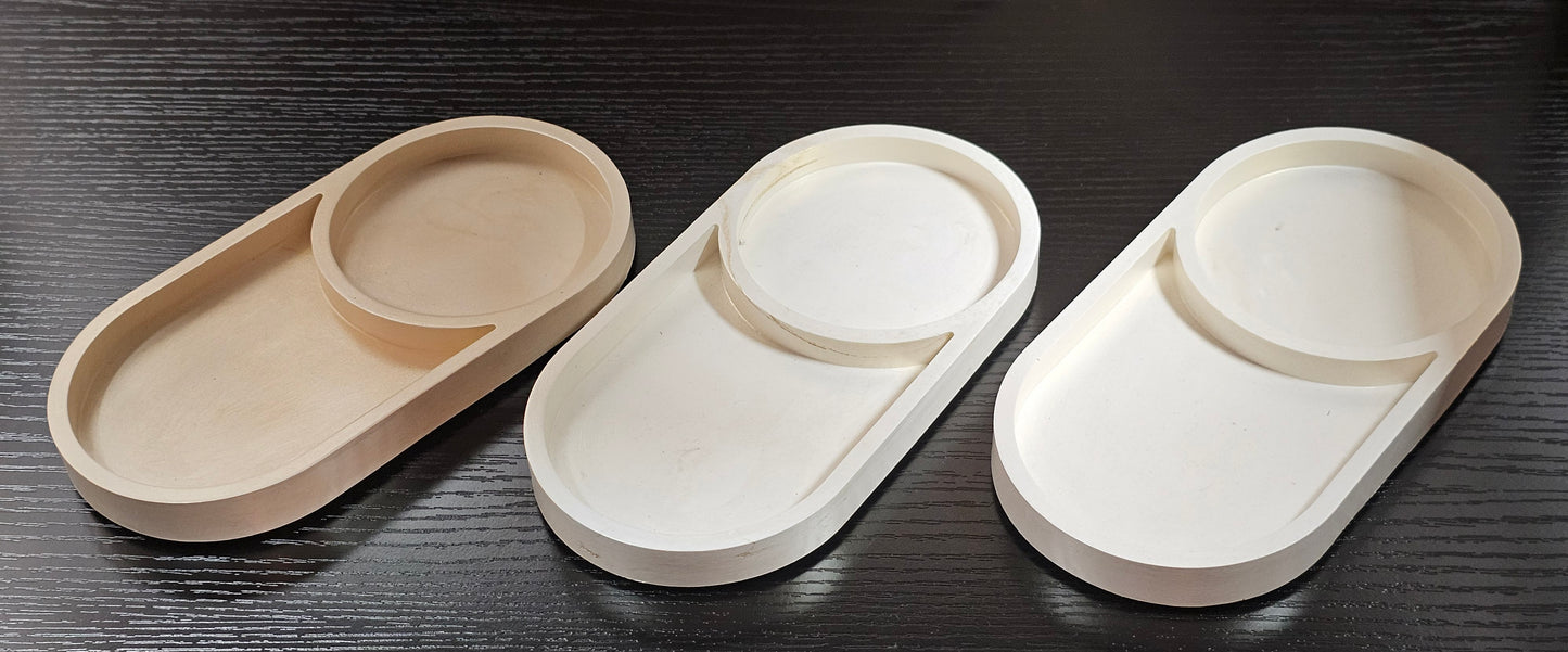Three oval trays in beige, white, and a light brown color on a dark wooden surface.