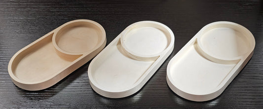 Three oval trays in beige, white, and a light brown color on a dark wooden surface.