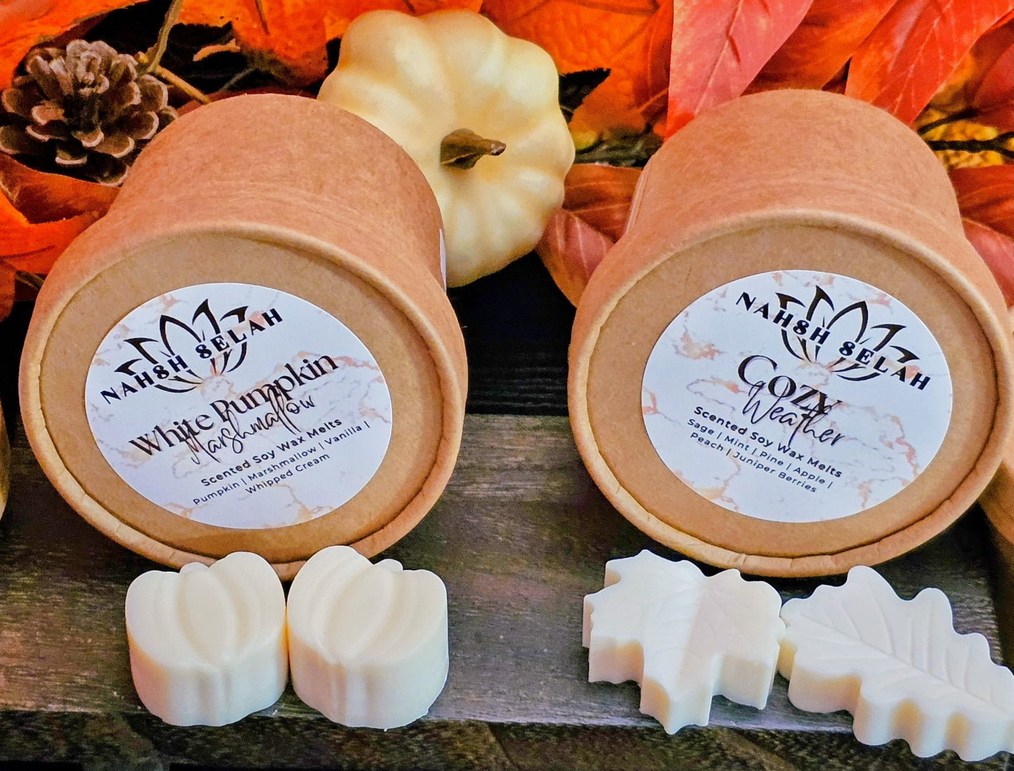Two containers of small pumpkin and leaf shaped wax melts on a wooden surface with autumn decorations.