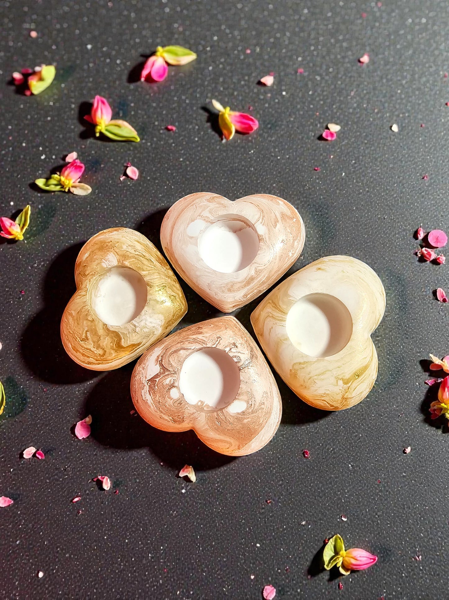 Heart-shaped candle holders on a dark surface with pink flower petals.