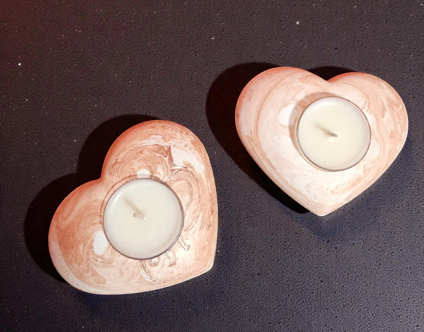 Two heart-shaped candle holders with candles on a dark surface