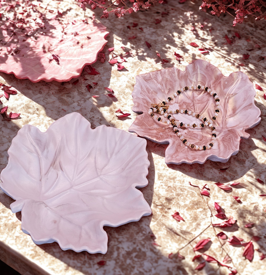 Pink leaf-shaped dish with a necklace on a textured surface with pink petals.