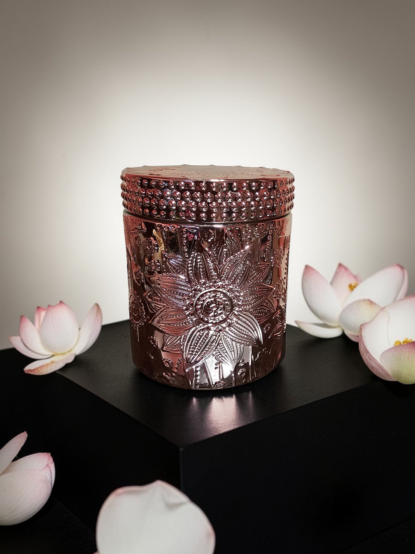 Decorative candle with floral design on a dark surface with pink flowers.