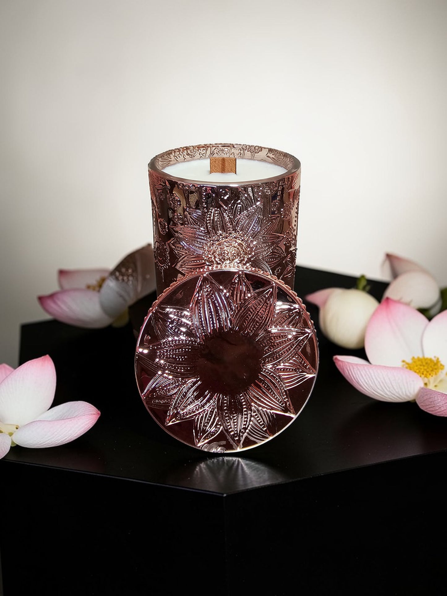 A candle in a rose gold vessel with lotus artwork.