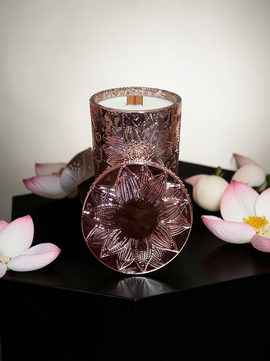 A candle in a rose gold vessel with lotus artwork.