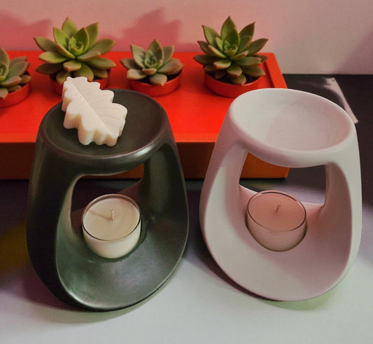 Two candle holders with candles inside, one black and one white, on a surface with succulents in the background.